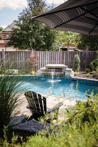 Backyard hardscaping with Armour Stone retaining walls and an inground swimming pool with a custom water feature.