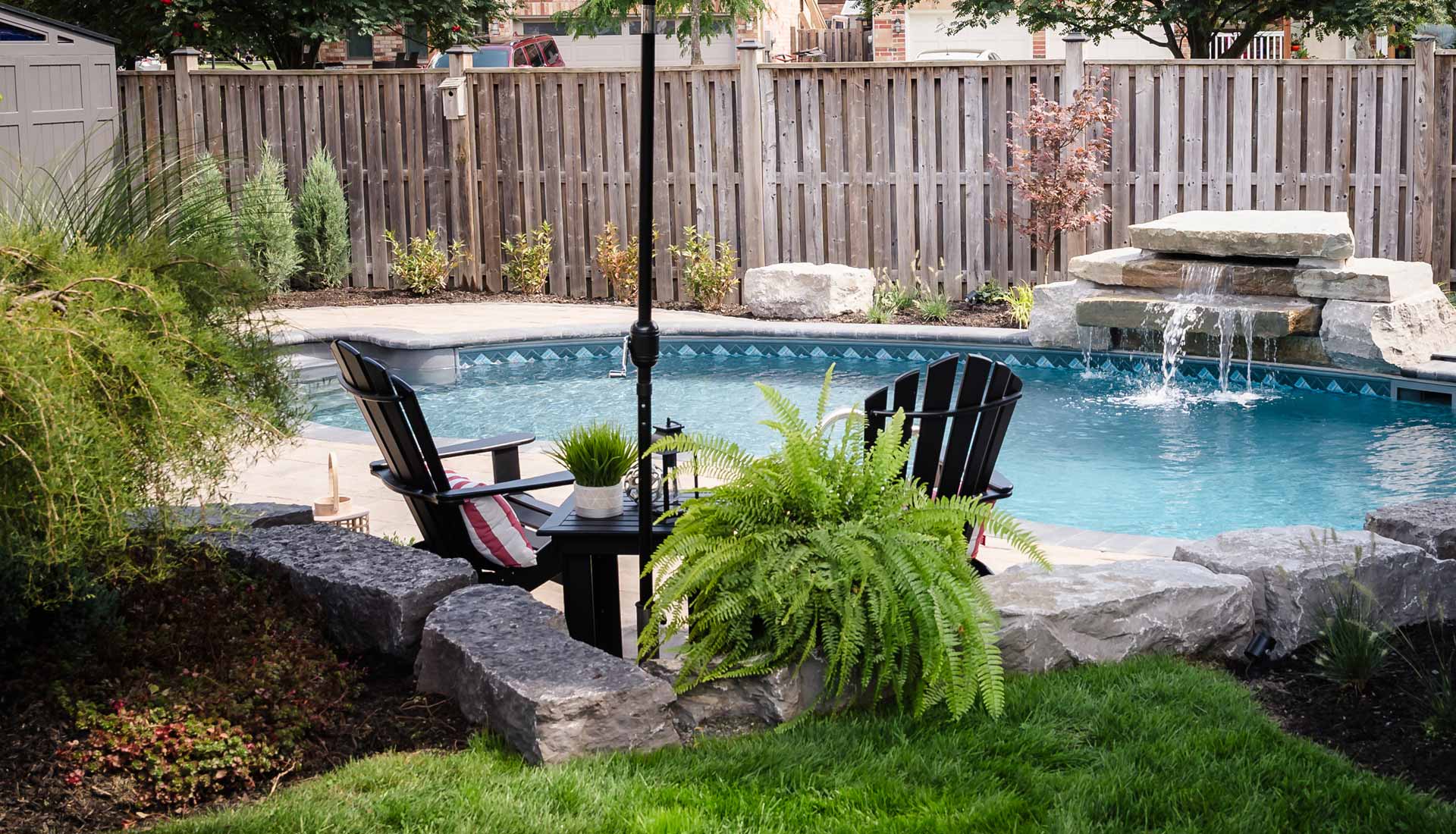 Backyard hardscaping with Armour Stone retaining walls and an inground swimming pool with a custom water feature.